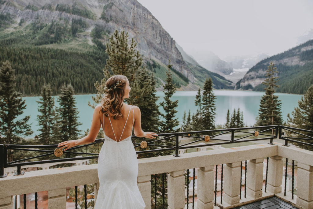 Bride looks at Lake Louise while on the terrace of the Fairmont Chateau in Lake Louise