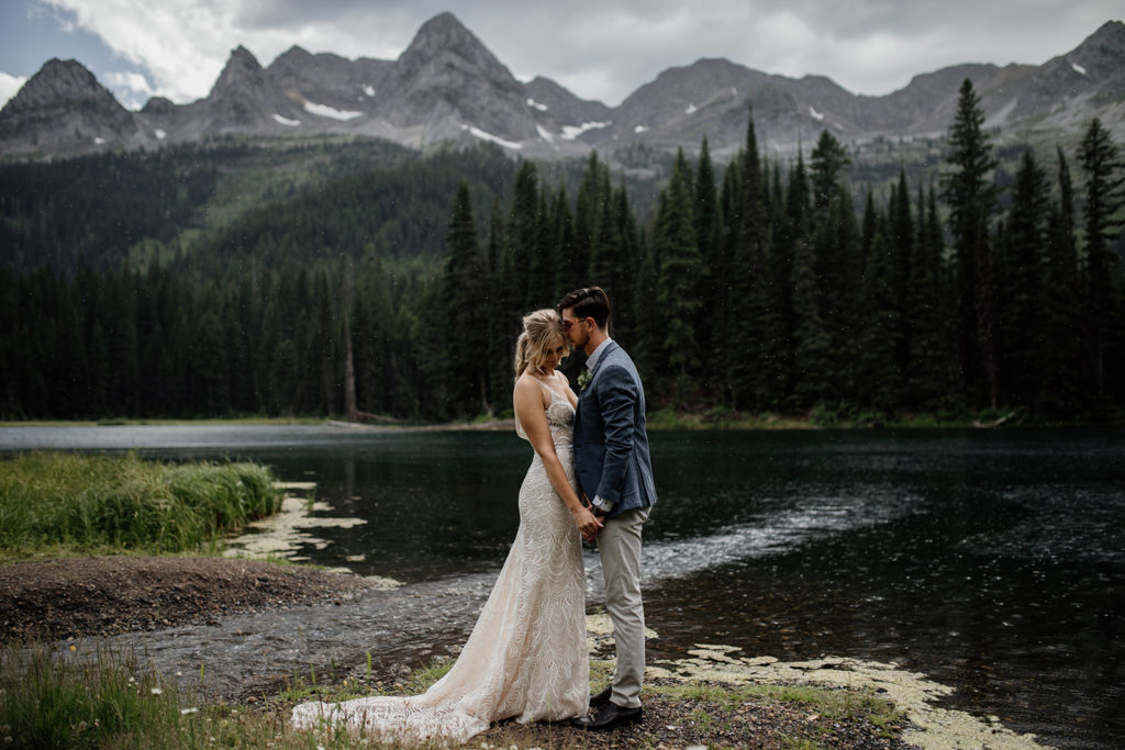 A bride and groom sharing an intimate moment, touching foreheads together in front of a moody backdrop of the mountains