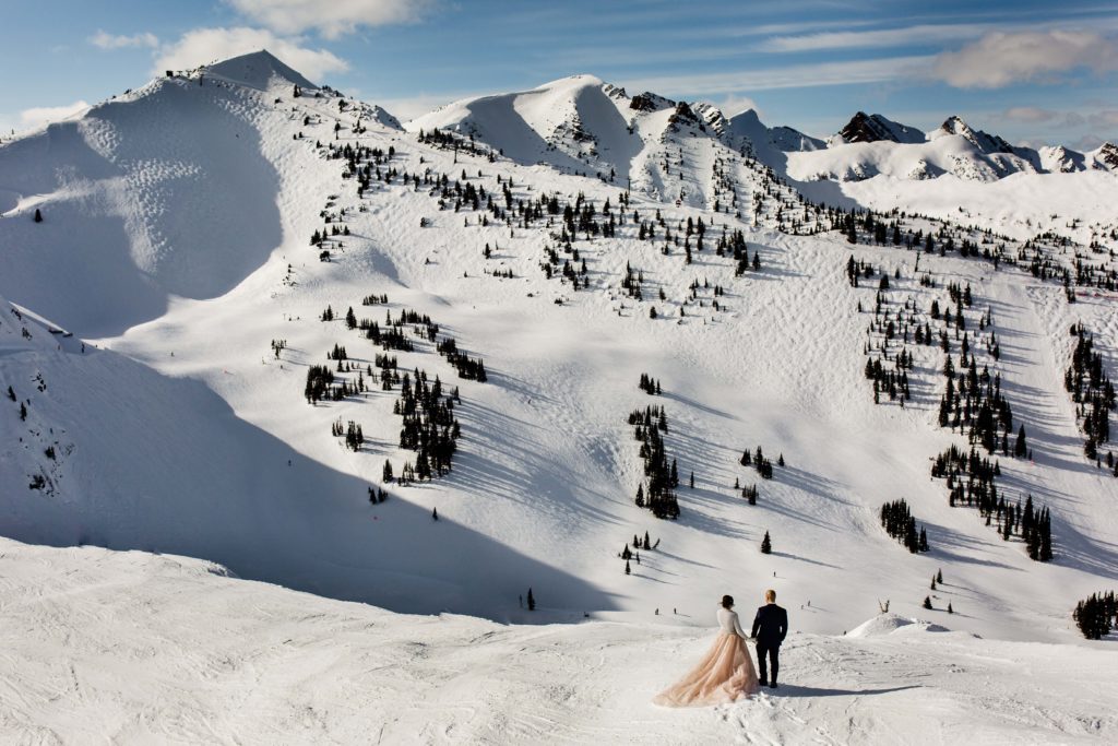 Wedding couple in winter on ski slope surrounded by mountains